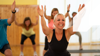 Lady in black squatting with arms stretched out with others spaced around her in a studio environment. Metafit is available at Dawlish Leisure Centre.