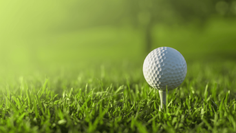 White golf ball on a tee with green grass surrounding it.