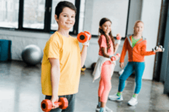 young boy with two young girls in the background holding weights in a junior gym session.