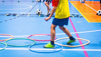 Child in yellow bib in a sports hall participating in a junior activity.