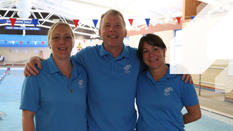 Three members of the team at Teignbridge Leisure by the swimming pool. Wearing blue tops with the Teignbridge Leisure Logo on the right side of the chest.